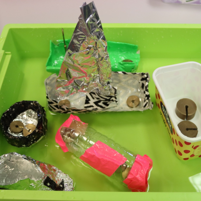 Early boat models being tested in a shallow container of water for buoyancy