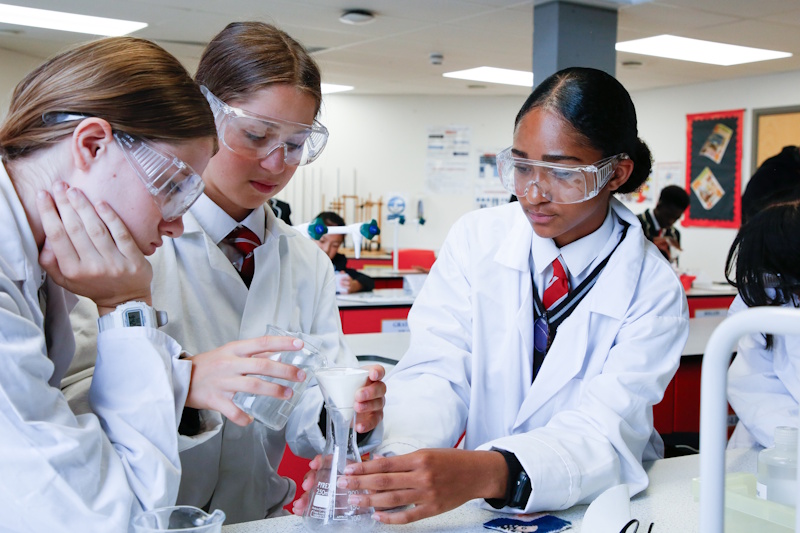 Three girls performing a science experiment in a classroom.