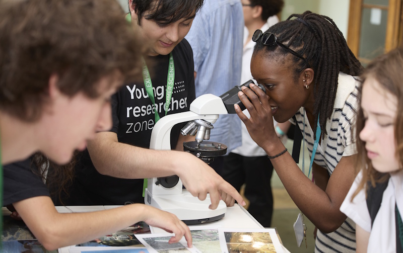 Young Researcher Zone students showing a visitor a slide through microscope 