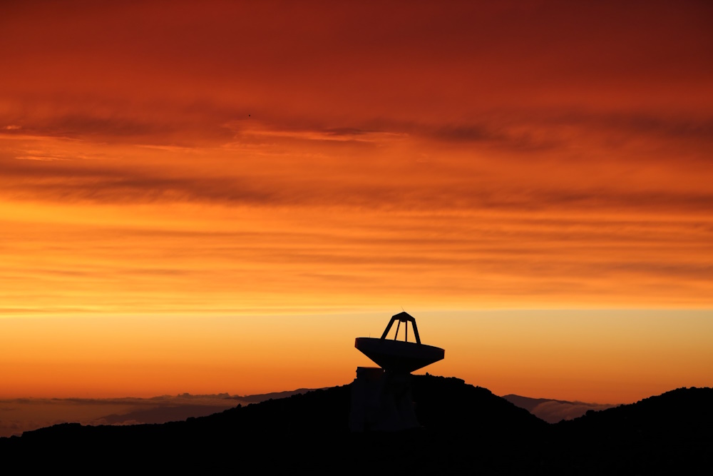 A large telescope in the midst of an orange sky.