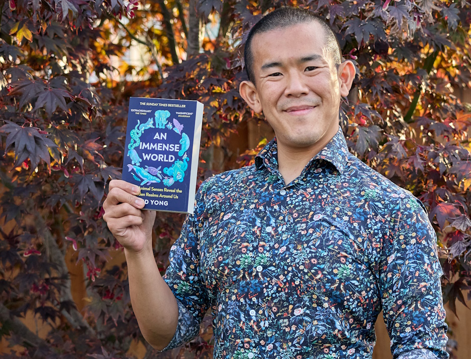 Author Ed Yong holding his book in front of a tree