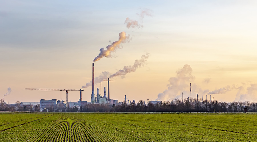 Industrial chimneys in front of green field.