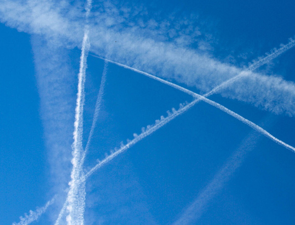 Image shows vapour trails from jet aircraft across a blue sky