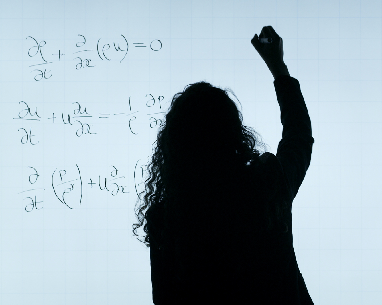 The image shows the silhouette of a woman with curly hair, illuminated against a whiteboard. She is writing an equation.