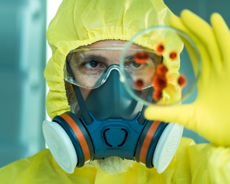 Man with yellow protective clothing and a gas mask looking into petri dish