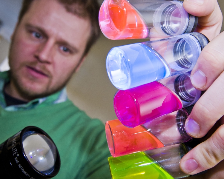 Man holding 5 test tubes full of brightly coloured, glowing liquid