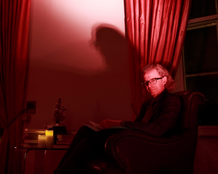 Man sitting in a room with red lighting, reading a book from the Royal Society's archives