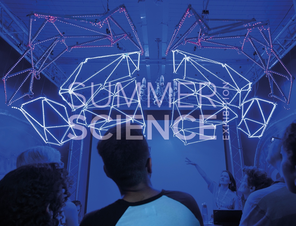 Summer Science Exhibition: a crowd viewing a light-up wire frame suspended from the ceiling of a room filled with deep blue light.