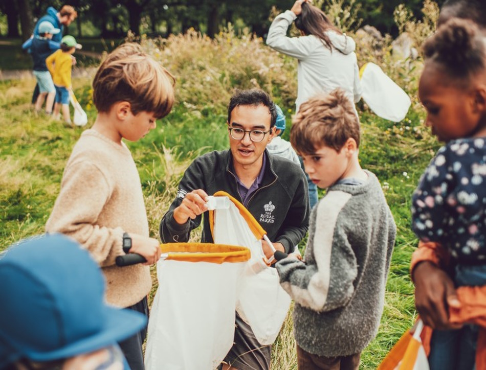 a man shows two young children a nature sample in a park