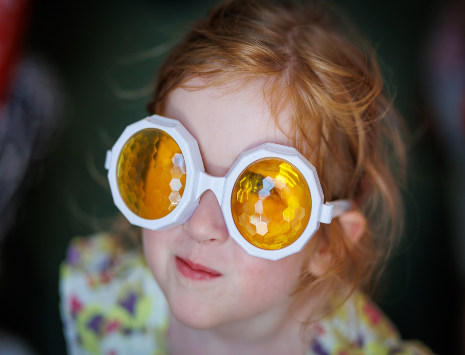 A young girl stares while wearing glasses with refracting orange lenses