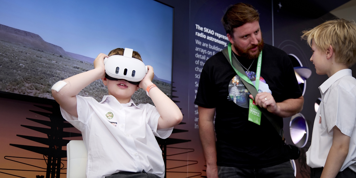 A boy wearing a VR headset whilst another talks to a scientist