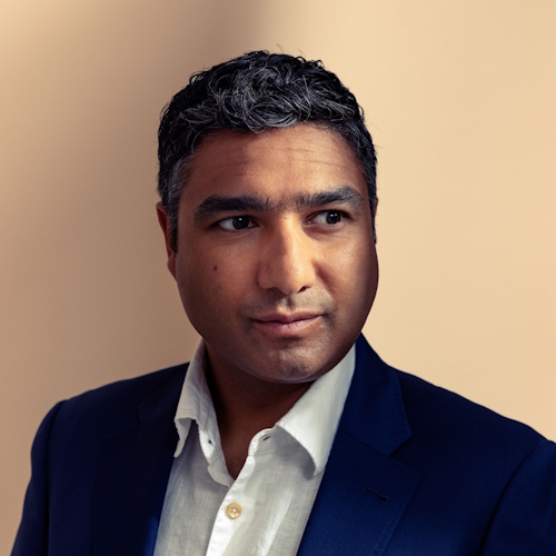 Nick Mohammed wearing a white shirt and navy blazer against cream background
