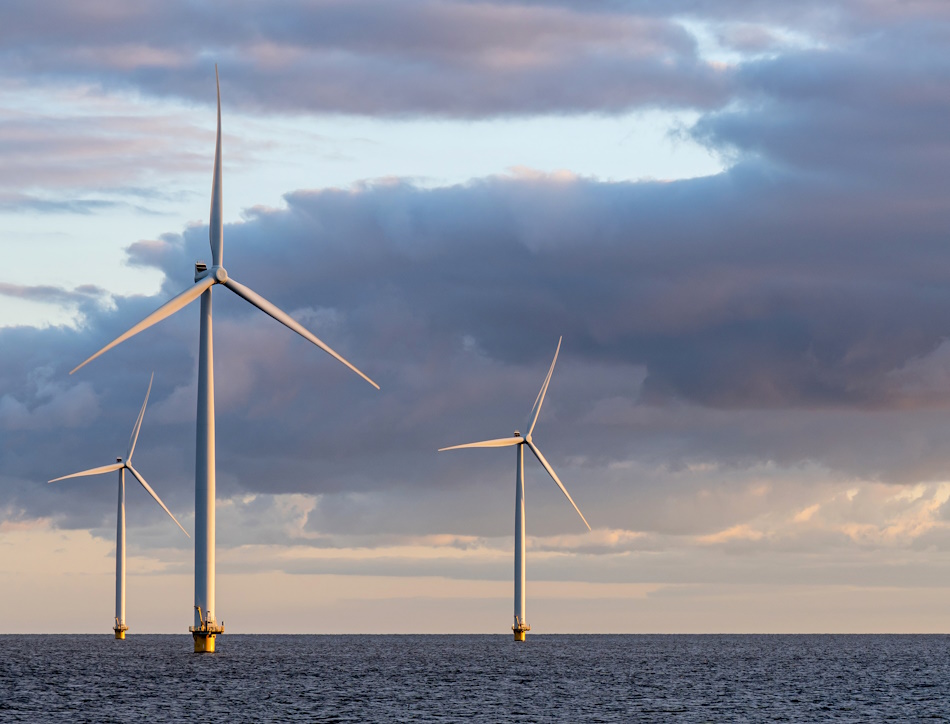 Offshore wind farm at dusk with clouds in the background.